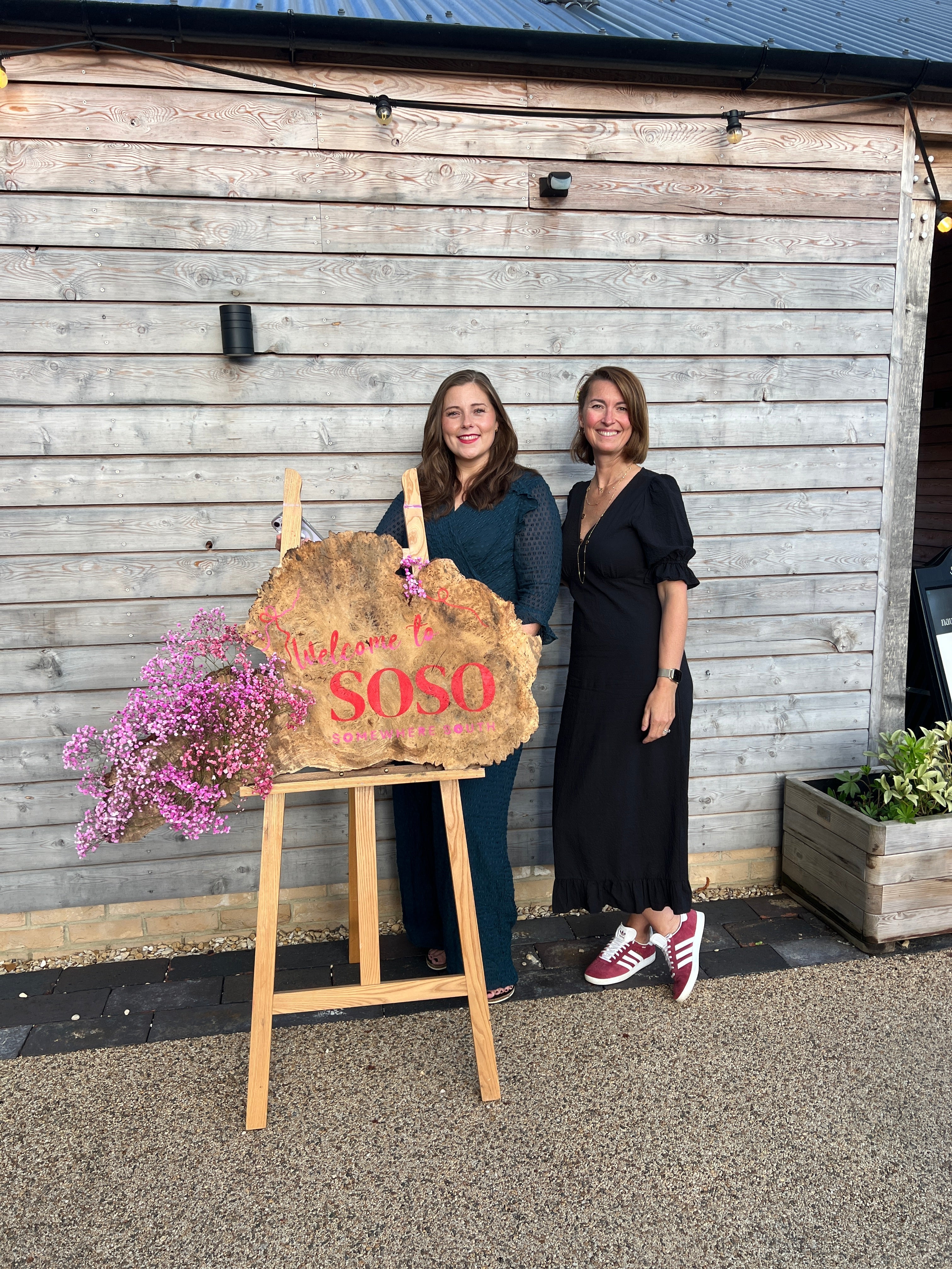 Cat & Emily standing in front of a wooden sign that says Welcome to SoSo