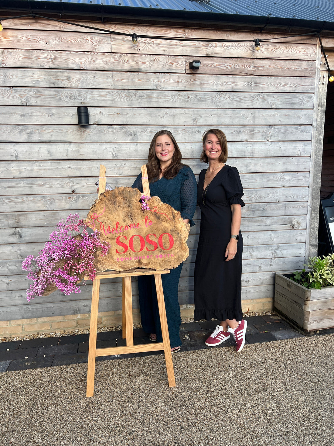 Cat & Emily standing in front of a wooden sign that says Welcome to SoSo